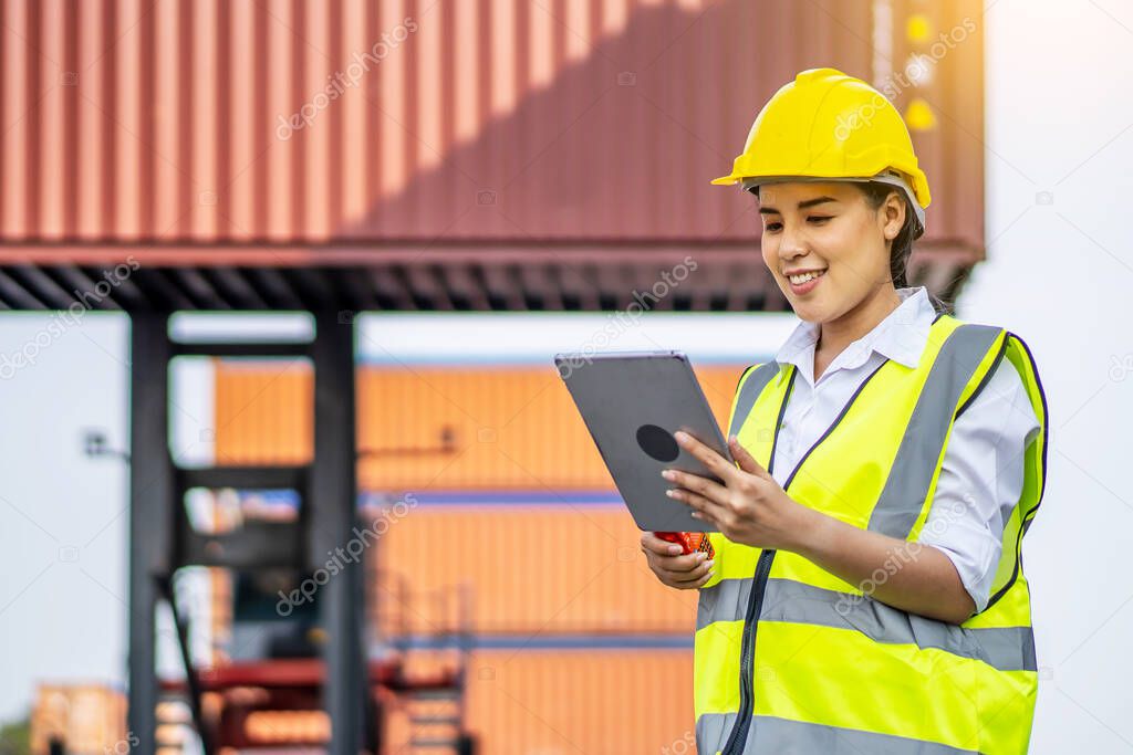Professional engineer container cargo woman in helmets smiled happily after successfully using the tablet to inspect the stock of export products and information in her business