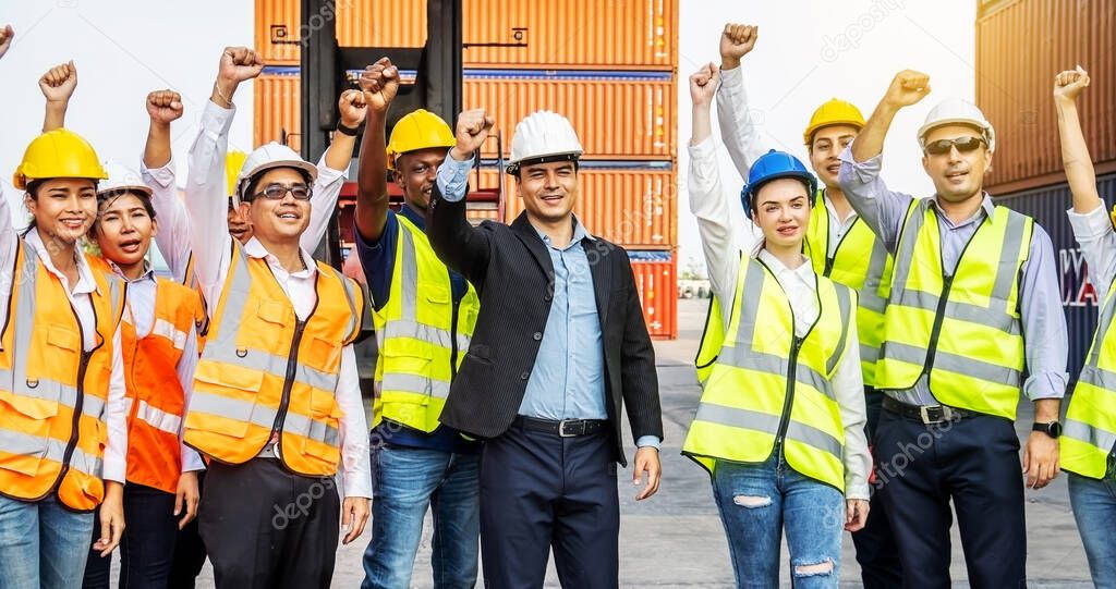 Cargo container workers or group of employee express raised their hands to express their joy to celebrate the success of their work. With a crane and a shipping container pile in the background