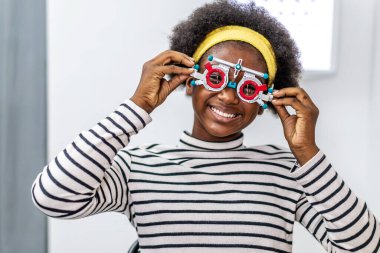 Smiling young woman african american checking vision with eye test glasses during a medical examination at the ophthalmological office, Checking eye vision by optician health examination concept