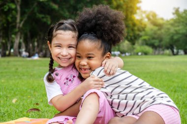 İki Afrikalı Amerikalı neşeli küçük kız paspasın üzerinde oturup birbirine sevgiyle sarılıyorlar.