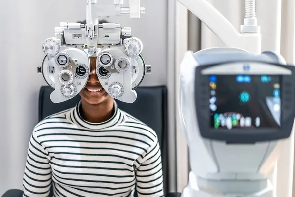 Smiling young woman african american afro hair doing Eye test on optical phoropter, checking on her eye with optometry machine