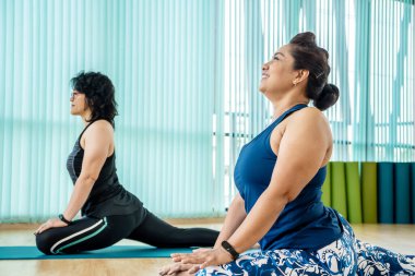 Birlikte yoga eğitimi alan kadınlar, spor salonunda bacağını mindere koyan gülümseyen kadınlar, sağlıklı yaşam tarzı ve fitness konsepti.