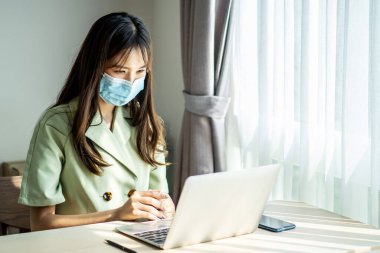 İş kadını, kendini tecrit ve karantina sırasında bilgisayarın başında çalışırken tıbbi koruyucu maske takıyor. Coronavirüs salgını ve covid salgını. Evde kal..