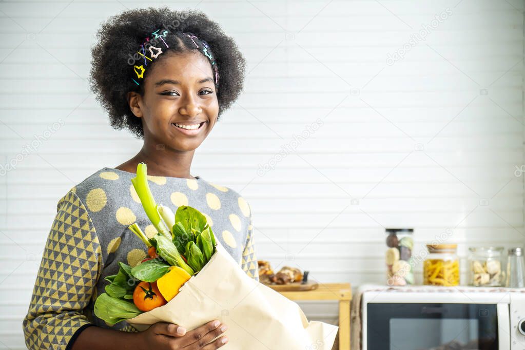 Happy healthy African american girl in the kitchen, Adorable girl smiling and holding paper bag with fresh food full of vegetables, Healthy eating