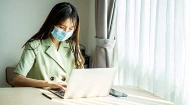 İş kadını, kendini tecrit ve karantina sırasında bilgisayarın başında çalışırken tıbbi koruyucu maske takıyor. Coronavirüs salgını ve covid salgını. Evde kal..