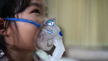 Solunum hastalığına yakalanan ve buharla tedavi edilen astım maskesi ile solunum tedavisi gören Asyalı hasta kız. 