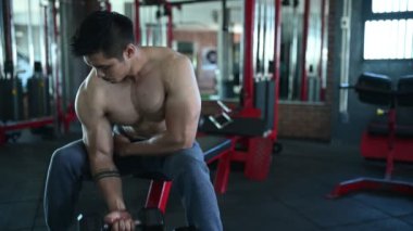 Büyük kaslı Asyalı adam spor salonunda ağırlık çalışması yapıyor.