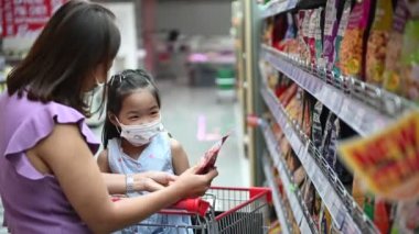 Maskeli Asyalı anne ve kız süpermarkette alışveriş yapıyorlar, covid-19 konsepti.