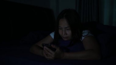 Geceleri yatakta akıllı telefon çalan Asyalı kadın.