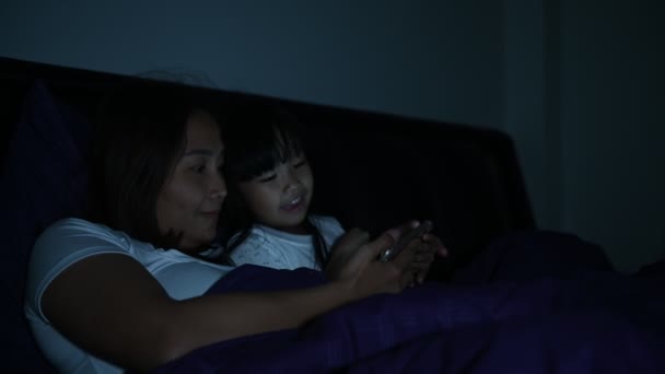 母と娘は夜にベッドでスマートフォンを — ストック動画