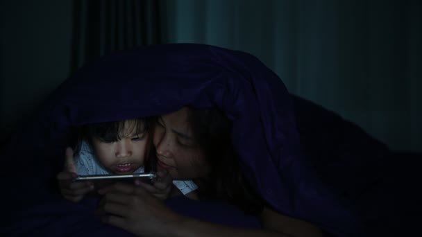 母と娘は夜にベッドでスマートフォンを — ストック動画
