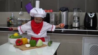 Mutfak odasındaki masada bir sürü sebze bulunan şef üniforması giyen tatlı Asyalı kız.