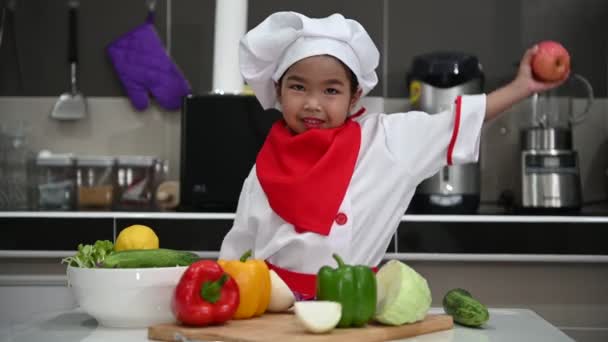 可愛いですアジアの女の子は キッチンルームでテーブルの上に野菜の多くとシェフの制服を着て — ストック動画