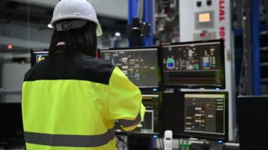 Yüksek performanslı bilgisayarlardaki mühendis bilgisayar işçisi büyük fabrikadaki monitörlerle büyük makinelerin çalışmasını kontrol ediyor.