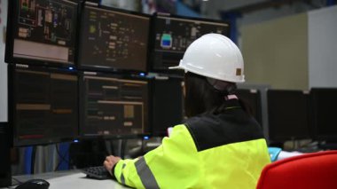 Yüksek performanslı bilgisayarlardaki mühendis bilgisayar işçisi büyük fabrikadaki monitörlerle büyük makinelerin çalışmasını kontrol ediyor.