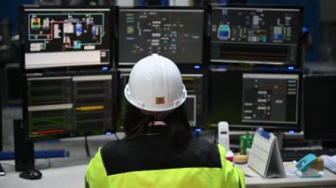 Yüksek performanslı bilgisayarlardaki mühendis bilgisayar işçisi büyük fabrikadaki monitörlerle büyük makinelerin çalışmasını kontrol ediyor.