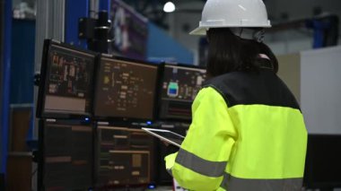 Yüksek performanslı bilgisayarlardaki mühendis bilgisayar işçisi büyük fabrikadaki monitörlerle büyük makinelerin çalışmasını kontrol ediyor.