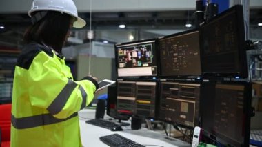 Yüksek performanslı bilgisayarlardaki mühendis bilgisayar işçisi büyük fabrikadaki monitörlerle büyük makinelerin çalışmasını kontrol ediyor.