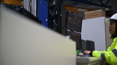 Yüksek performanslı bilgisayarlardaki mühendis bilgisayar işçisi büyük fabrikadaki monitörlerle büyük makinelerin çalışmasını kontrol ediyor.