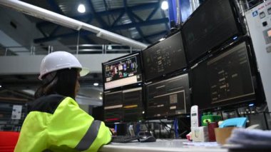 Yüksek performanslı bilgisayarlardaki mühendis bilgisayar işçisi büyük fabrikadaki monitörlerle büyük makinelerin çalışmasını kontrol ediyor.