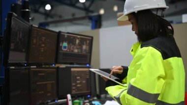 Yüksek performanslı bilgisayarlardaki mühendis bilgisayar işçisi büyük fabrikadaki monitörlerle büyük makinelerin çalışmasını kontrol ediyor.