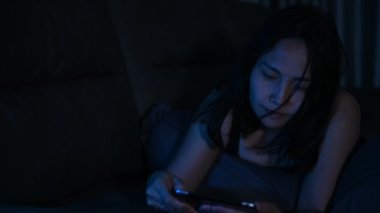 Gece yatakta akıllı telefonlarla oyun oynayan Asyalı kadın, sosyal medya bağımlılığı kavramı.