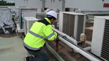 Klima teknisyeni binanın dışındaki birimleri tamir ediyor ve muhafaza ediyor.