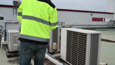Klima teknisyeni binanın dışındaki birimleri tamir ediyor ve muhafaza ediyor.