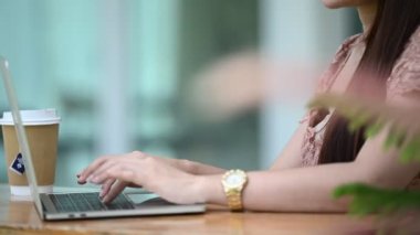 Genç Asyalı kadın kafede otururken dizüstü bilgisayarda çalışıyor.