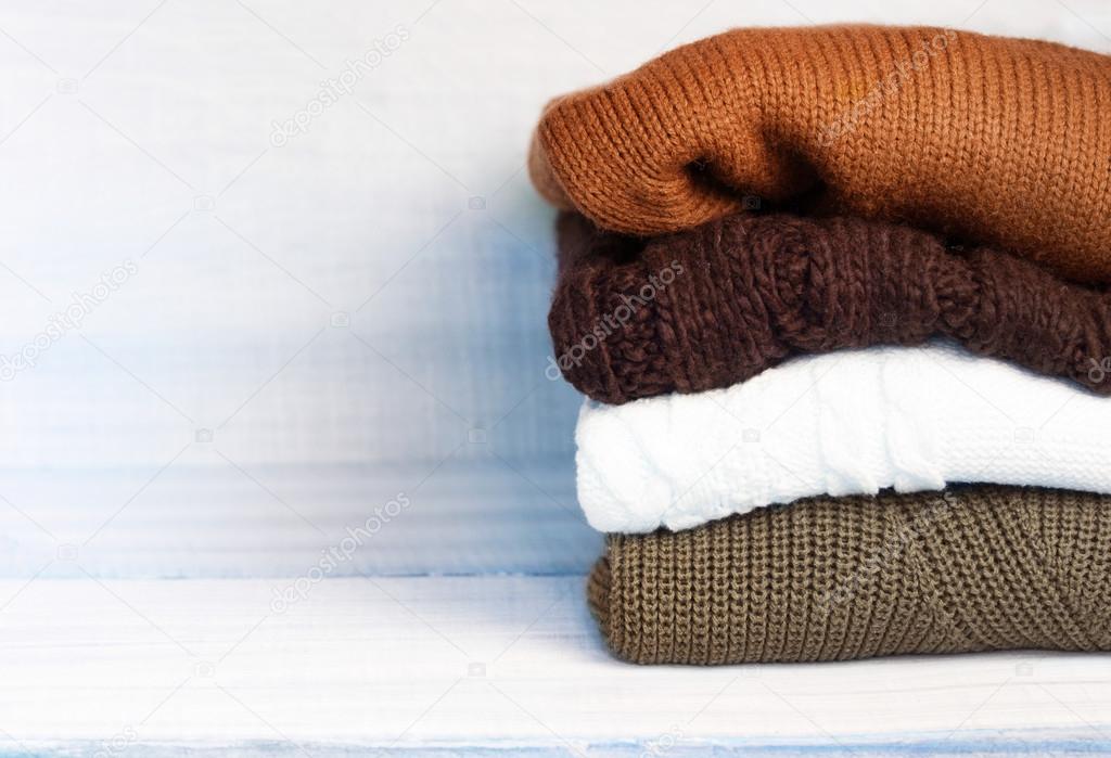 Pile knitted winter autumn clothes on wooden background.