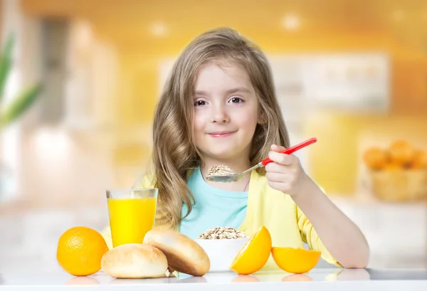 Kind meisje eten bij tabel granen oranje sap binnenshuis. — Stockfoto