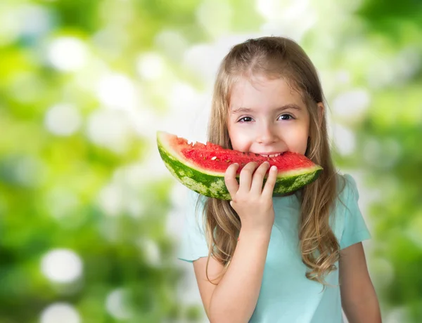 Barn flicka äter skiva vattenmelon på gröna oskärpa bakgrund. — Stockfoto