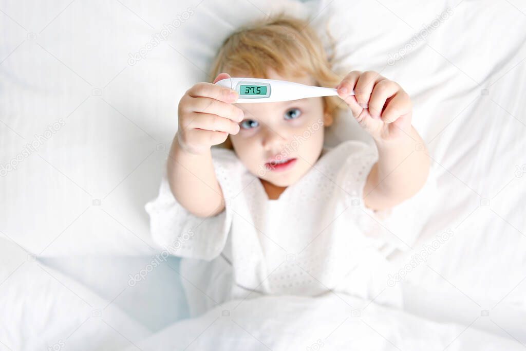 Caucasian child girl in bed with thermometer,kid with temperature lying ill.