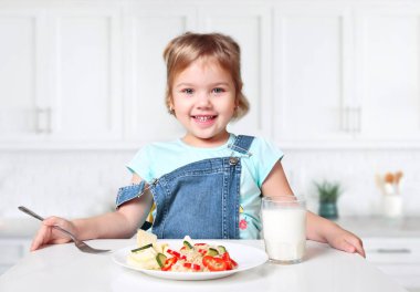 Masada bir tabak yemek ve bir bardak süt ile gülümseyen küçük bir çocuk. Çocuğun evde yemeği var. Kafkasyalı küçük kız taze sebzeli pilav yiyor, sağlıklı beslenme kavramı var..
