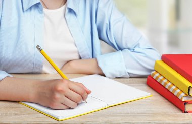 Kalemle kitap yazan kız çocuğu. Masadaki öğrenci, bir yığın kitap. Okul ödevi. Çocuğun çalışma süreci. Eğitim kavramı.