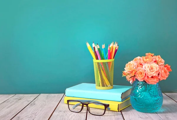 Teacher\'s day. Knowledge day concept. Stack of books,pencils,glasses and flowers vase on table with empty green blue background.