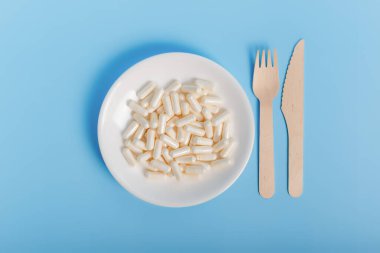 Besin takviyesi tabağı ve arka planda mineral kompleks vitaminler. Ek maddeler ve minerallerle düz bileşim. Besin takviyesi yeme zamanı. Mavi arkaplanda beyaz plaka