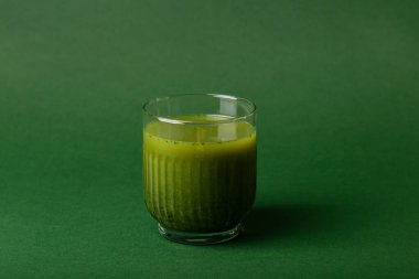 Bir bardak sağlıklı meyve suyu. Yeşil arka planda ananas, kivi, ıspanak ve muzdan yapılmış bir bardak smoothie.. 