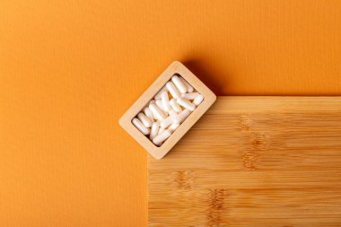Besleyici maddeler, vitaminler ve mineraller. Beyaz vitamin hapları ahşap kutuda. Yukarıdan, turuncu arka plandaki ahşap bir masada. Sağlıklı yaşam tarzı