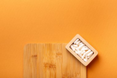 Besleyici maddeler, vitaminler ve mineraller. Beyaz vitamin hapları ahşap kutuda. Yukarıdan, turuncu arka plandaki ahşap bir masada. Sağlıklı yaşam tarzı