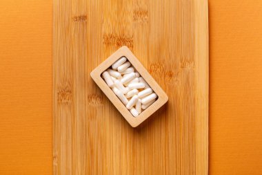 Besleyici maddeler, vitaminler ve mineraller. Beyaz vitamin hapları ahşap kutuda. Yukarıdan, turuncu arka plandaki ahşap bir masada. Sağlıklı yaşam tarzı