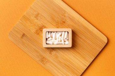 Besleyici maddeler, vitaminler ve mineraller. Beyaz vitamin hapları ahşap kutuda. Yukarıdan, turuncu arka plandaki ahşap bir masada. Sağlıklı yaşam tarzı