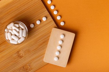 Besleyici maddeler, vitaminler ve mineraller. Yukarıdan gelen beyaz vitamin hapları turuncu arka plandaki ahşap bir masada. Sağlıklı yaşam tarzı