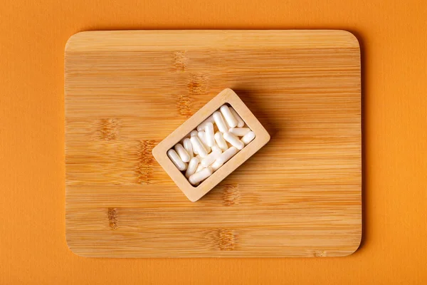Besleyici maddeler, vitaminler ve mineraller. Beyaz vitamin hapları ahşap kutuda. Yukarıdan, turuncu arka plandaki ahşap bir masada. Sağlıklı yaşam tarzı