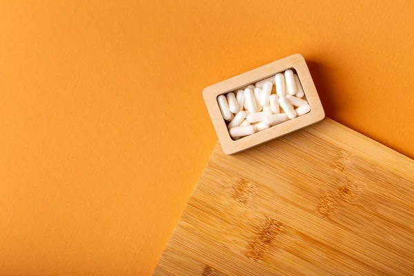 Besleyici maddeler, vitaminler ve mineraller. Beyaz vitamin hapları ahşap kutuda. Yukarıdan, turuncu arka plandaki ahşap bir masada. Sağlıklı yaşam tarzı
