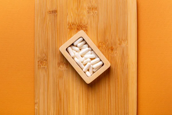 Besleyici maddeler, vitaminler ve mineraller. Beyaz vitamin hapları ahşap kutuda. Yukarıdan, turuncu arka plandaki ahşap bir masada. Sağlıklı yaşam tarzı