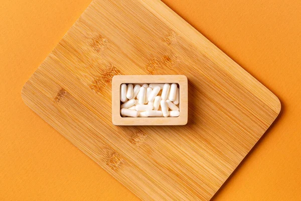 Besleyici maddeler, vitaminler ve mineraller. Beyaz vitamin hapları ahşap kutuda. Yukarıdan, turuncu arka plandaki ahşap bir masada. Sağlıklı yaşam tarzı