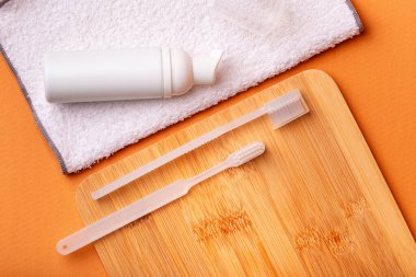 Ahşap masada beyaz diş fırçaları, diş macunu ve turuncu arka planda yüz havlusu. Ağız bakımı, sakız ve diş sağlığı. Sabah rutini ve diş bakımı.