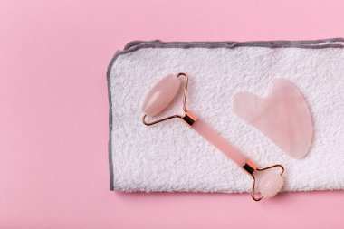 Yüz masajcısı ve pembe arka planda yüz havlusu. Güzellik ayinleri..