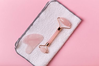 Yüz masajcısı ve pembe arka planda yüz havlusu. Güzellik ayinleri..